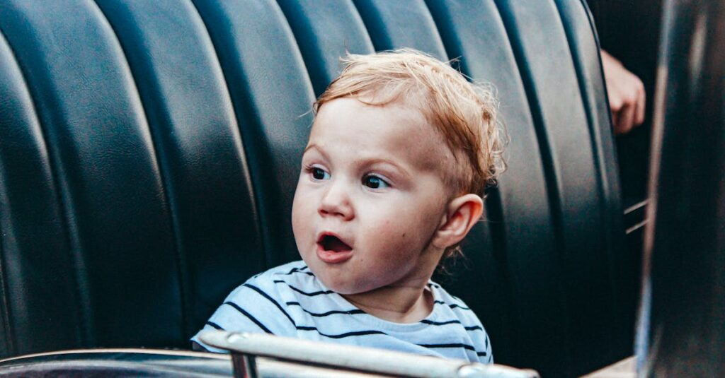 Cute child with surprised expression sitting in a car seat wearing a striped shirt.